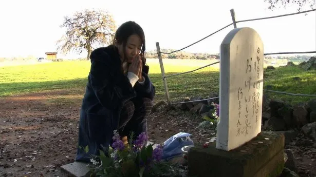 【写真を見る】農場跡地にある、おけいの墓を訪れ、手を合わせる鈴木聖奈