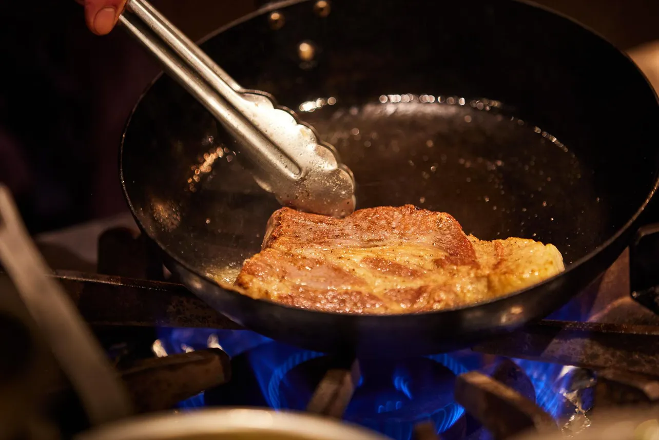 分厚い肩ロース肉をじっくり、こんがりと焼いていく　