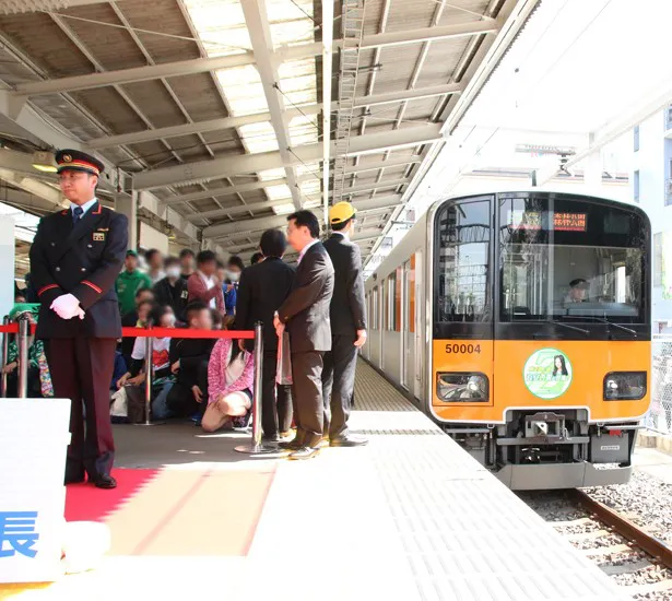 有安が1日駅長就任あいさつをしていると、有安デザインのヘッドマークを掲出した「ももいろ号」が入線