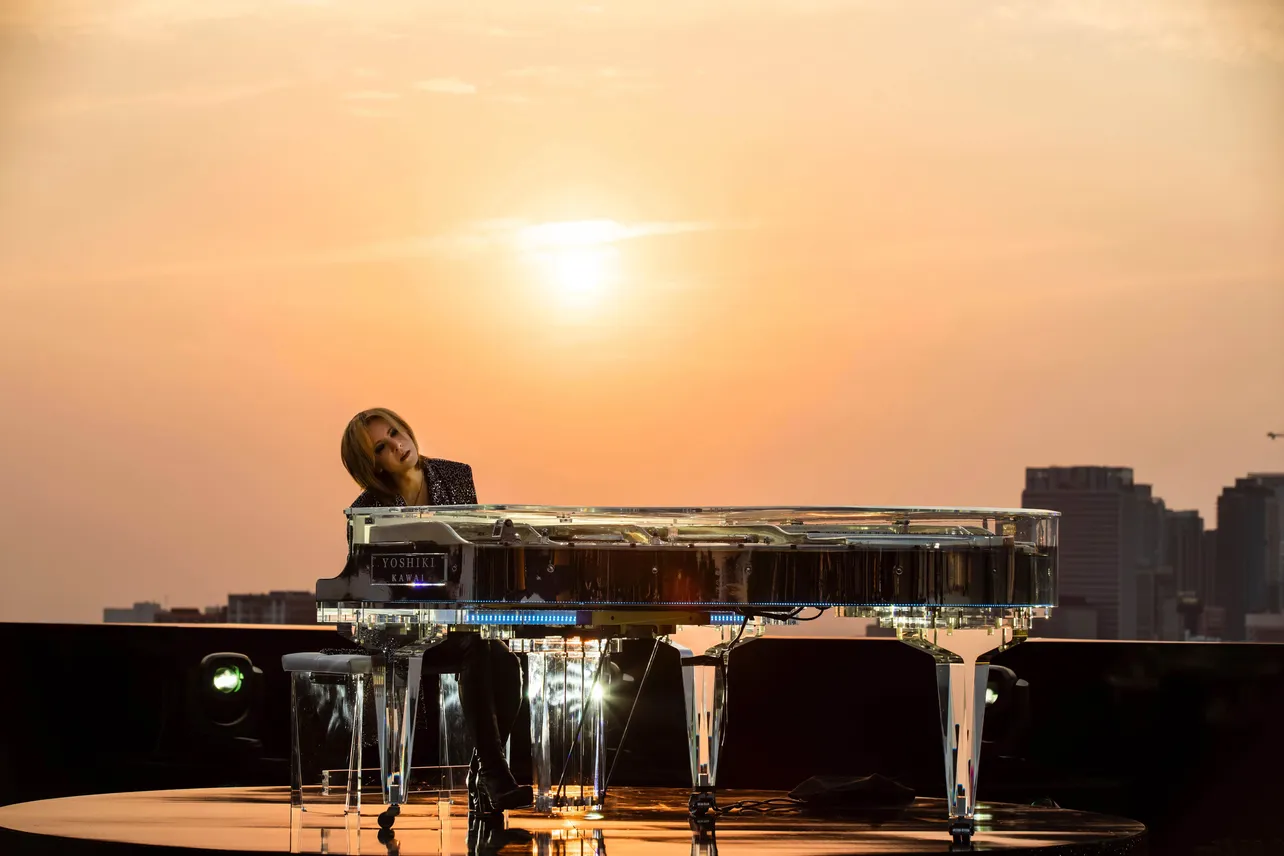 【写真】夕陽をバックにピアノを演奏するYOSHIKI