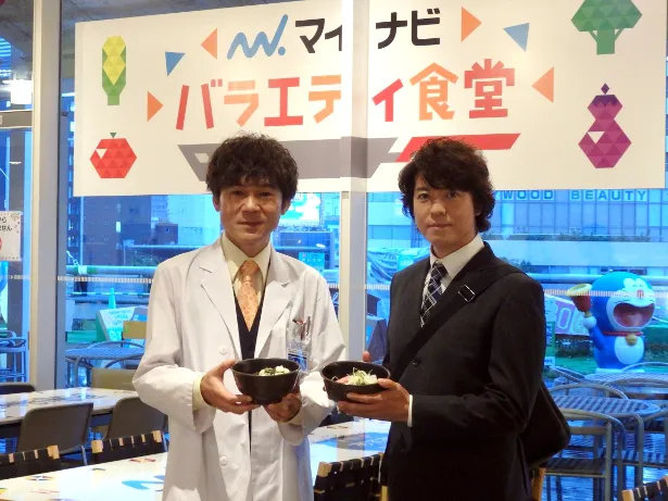 上川隆也(写真右)と甲本雅裕(写真左)は、「おいしい！」と絶賛のコラボメニュー“遺留そば”をアピール！
