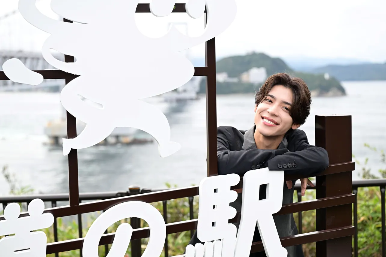 うず助のモチーフである鳴門海峡、大鳴門橋、淡路島の海をバックにニコニコの松島