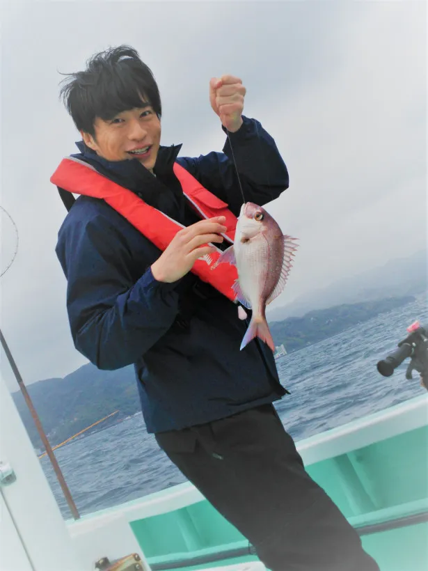 魚を釣り上げ、思わず笑顔を見せる田中