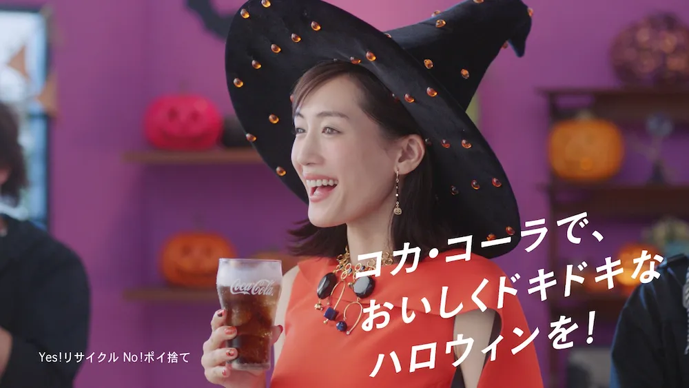 オレンジのワンピ ースに黒い帽子を合わせた魔女ルックでコカ・コーラを飲む綾瀬