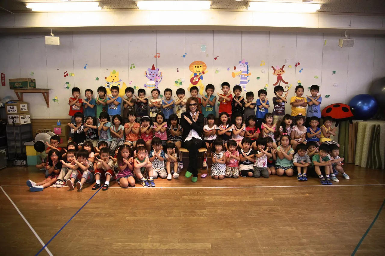 【写真を見る】大勢の子どもたちと一緒に“Xポーズ”をするYOSHIKI