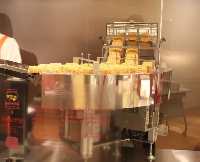 「マイカップヌードルファクトリー」のカップヌードルの麺をカップにセットする工程