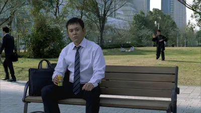 【写真】サラリーマン役の有田哲平が公園のベンチで休憩