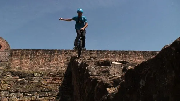 一輪車で断崖絶壁の城壁の上を一輪車で走行する冒険家が登場