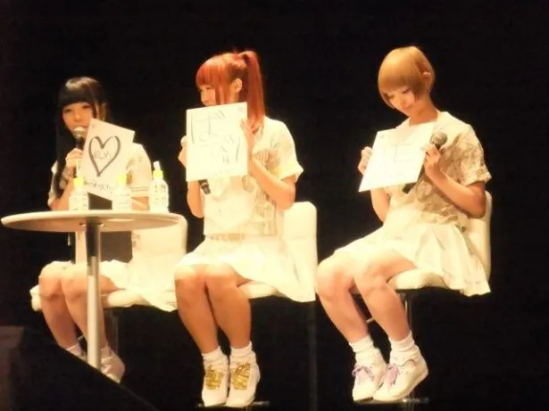 来場者へプレゼントする直筆色紙の説明をする相沢梨紗(左)、成瀬瑛美(中央)、最上もが(右)