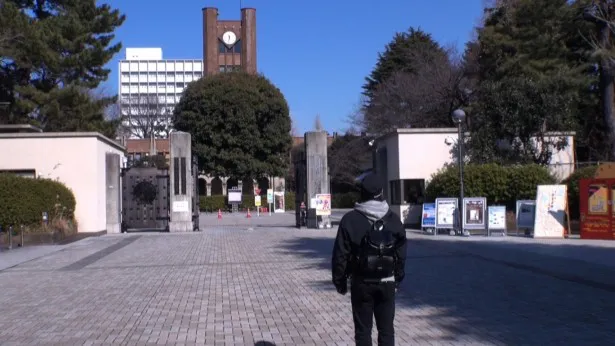 東京大学の門の前に立つラサール石井
