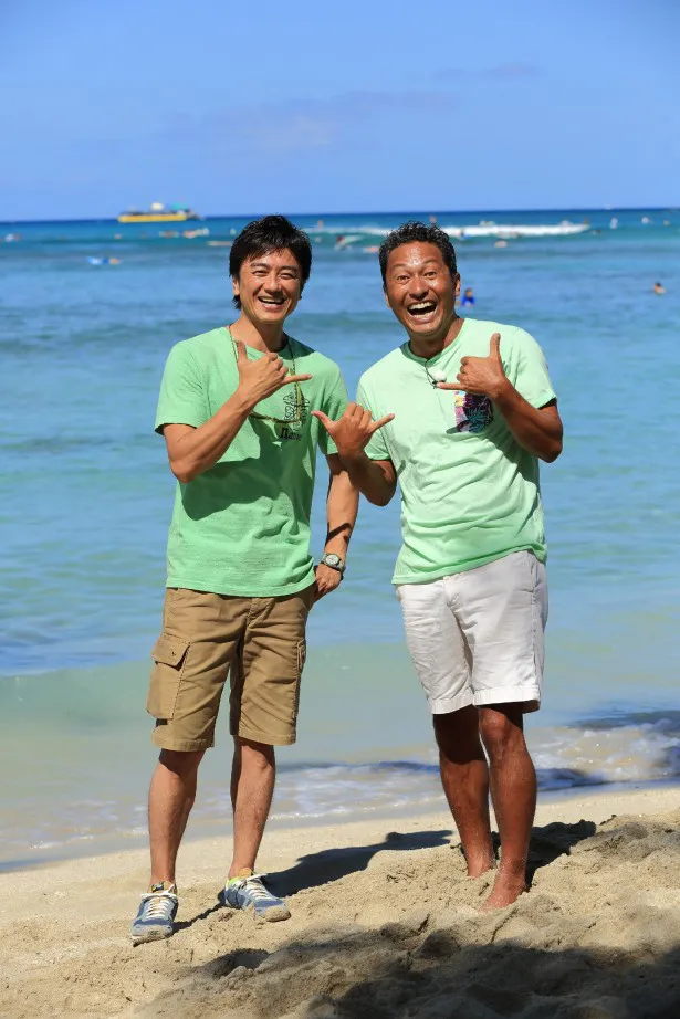 原田龍二が、ナビゲーターの内野亮(右)とハワイでおなじみの親指と小指を立てて手の甲を見せるハンドサインでメッセージ