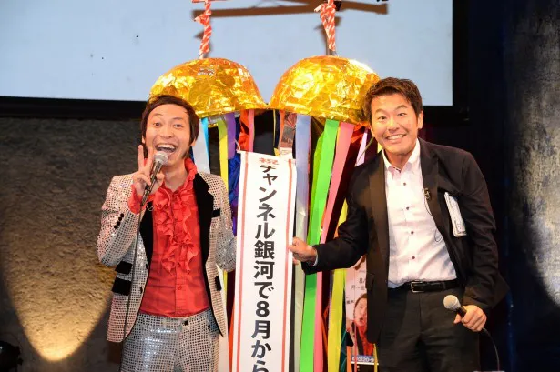 くす玉を割って全国放送を祝う上杉周大（左）と司会の横井健一（右）